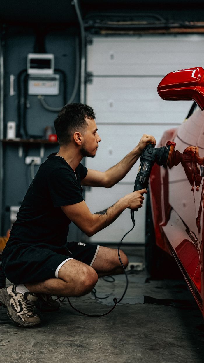 Man polishing a red sports car in a garage setting, demonstrating car detailing.