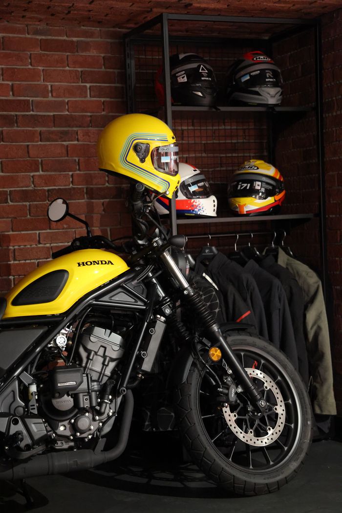 Vibrant yellow Honda motorcycle parked indoors surrounded by helmets and jackets.