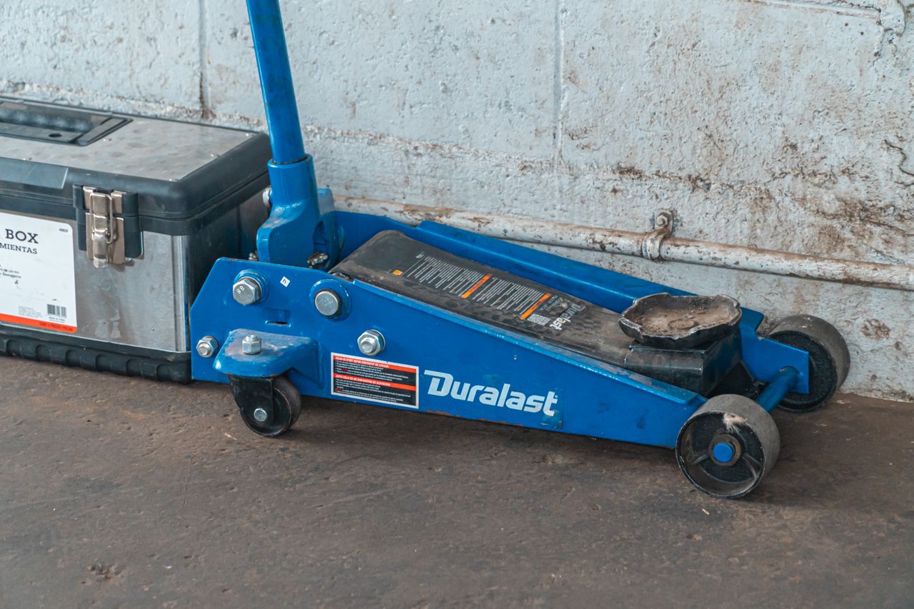 A blue hydraulic floor jack with a toolbox in an automotive garage setting.